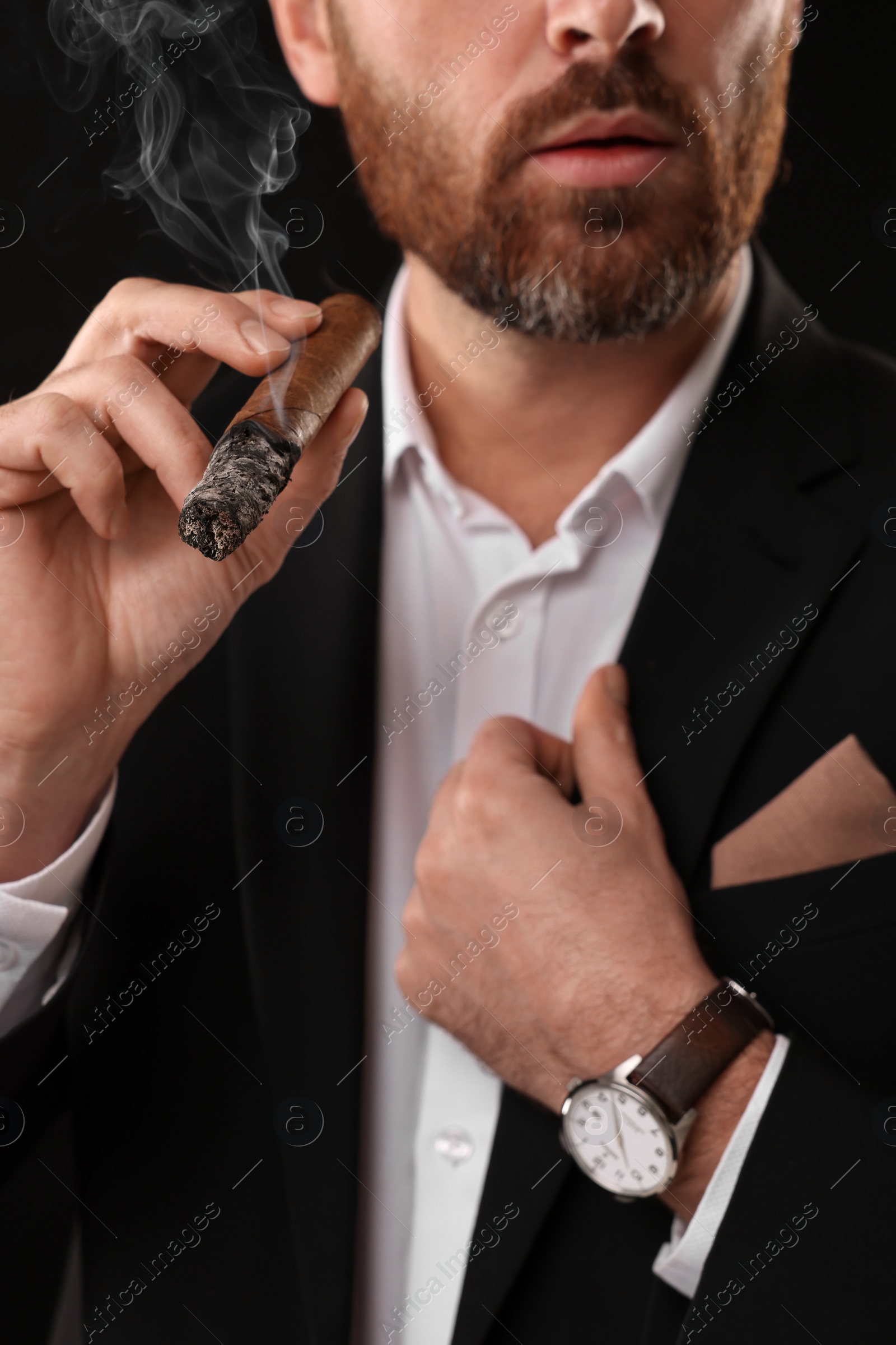 Photo of Man in elegant suit smoking cigar on black background, closeup