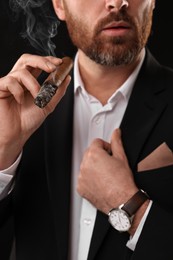 Man in elegant suit smoking cigar on black background, closeup