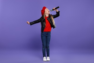 Photo of Cute little girl with microphone singing on purple background