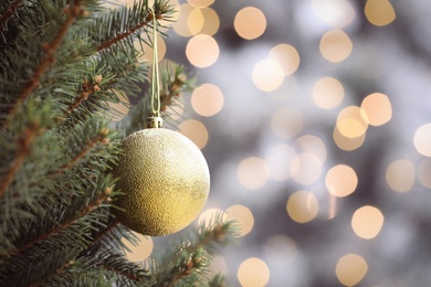 Shiny green ball hanging on Christmas tree against festive lights. Space for text