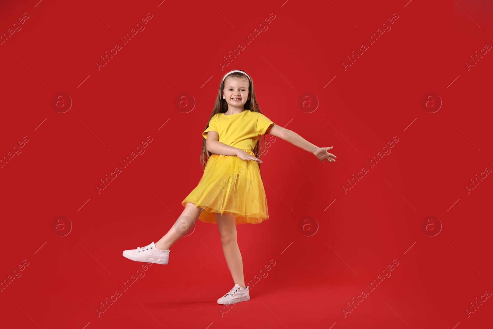 Photo of Cute little girl dancing on red background