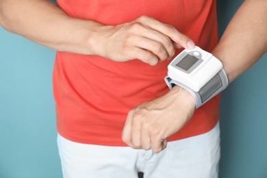 Young man checking pulse with blood pressure monitor on wrist against color background, closeup