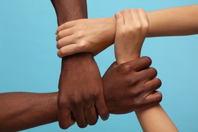 Photo of Woman and African American man joining hands together on light blue background, closeup