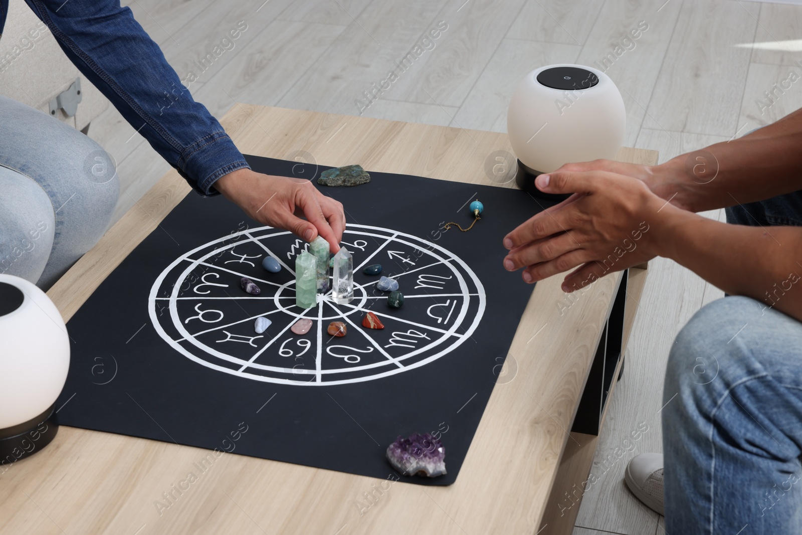 Photo of Astrologer predicting client's future with zodiac wheel, stones and crystals at wooden table indoors, closeup