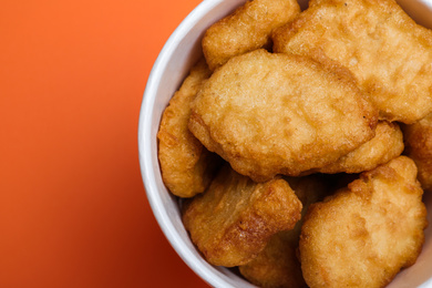 Photo of Bucket with delicious chicken nuggets on orange background, top view