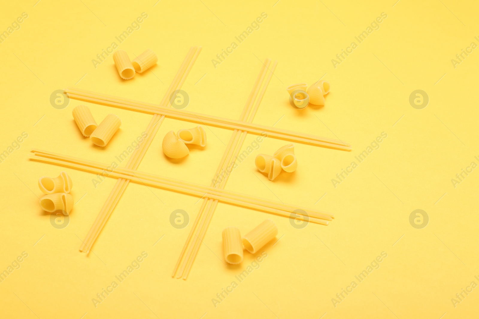Photo of Tic tac toe game made with different types of pasta on yellow background