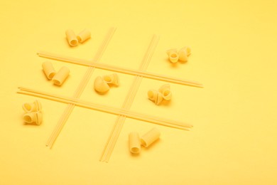 Tic tac toe game made with different types of pasta on yellow background