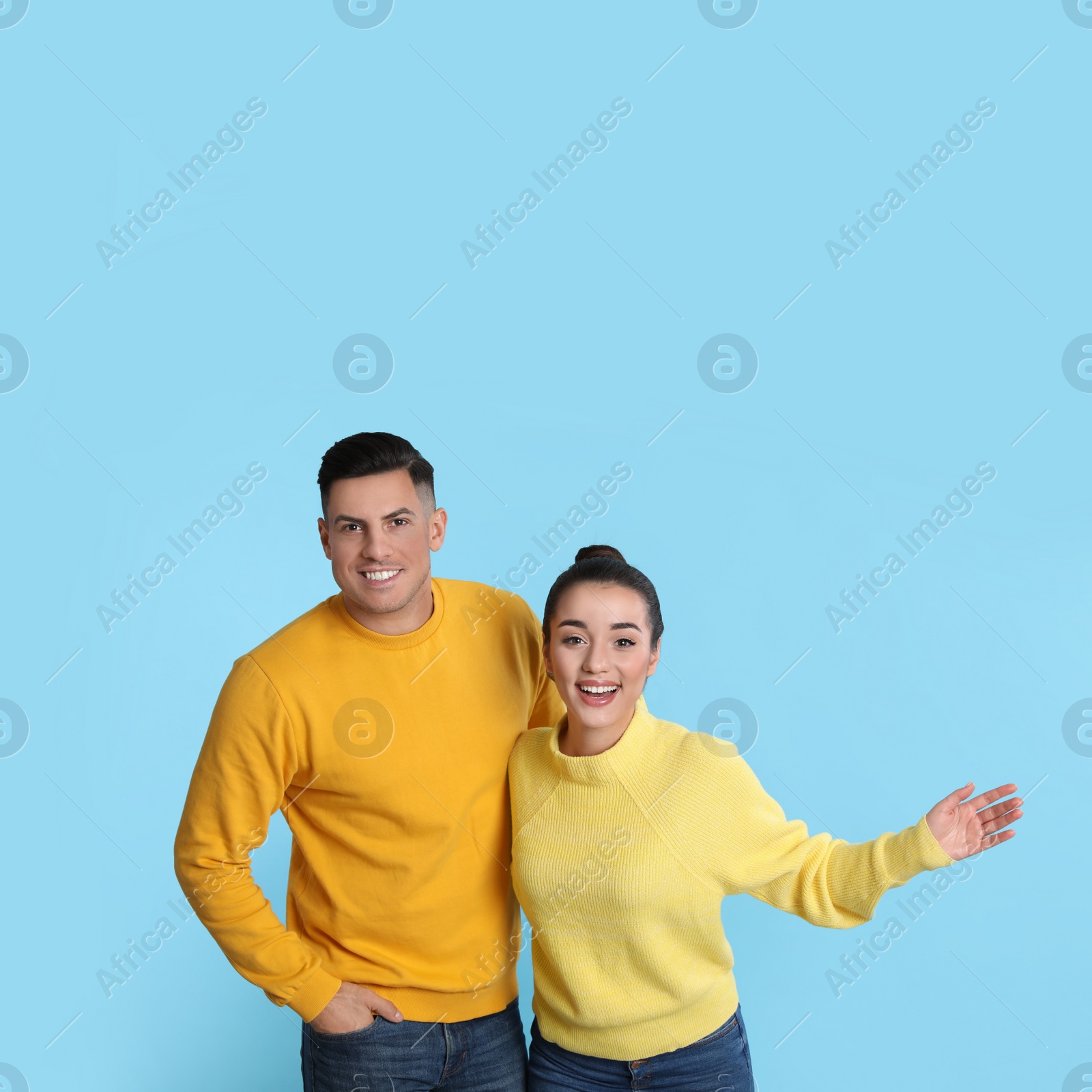 Photo of Happy couple wearing yellow warm sweaters on light blue background. Space for text