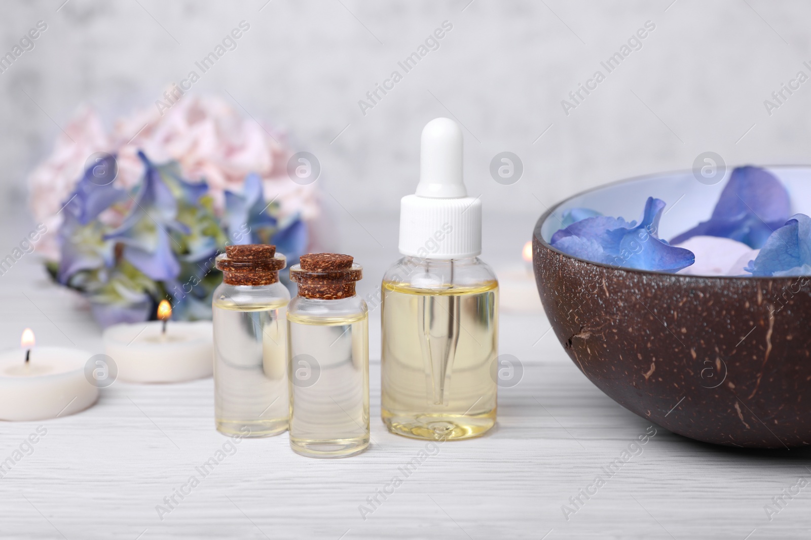 Photo of Spa composition. Bottles of essential oil and aromatic water with flowers in bowl on white wooden table, closeup