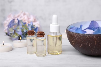 Spa composition. Bottles of essential oil and aromatic water with flowers in bowl on white wooden table, closeup