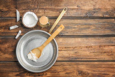 Photo of Frying pan with coconut oil and nut pieces on wooden background