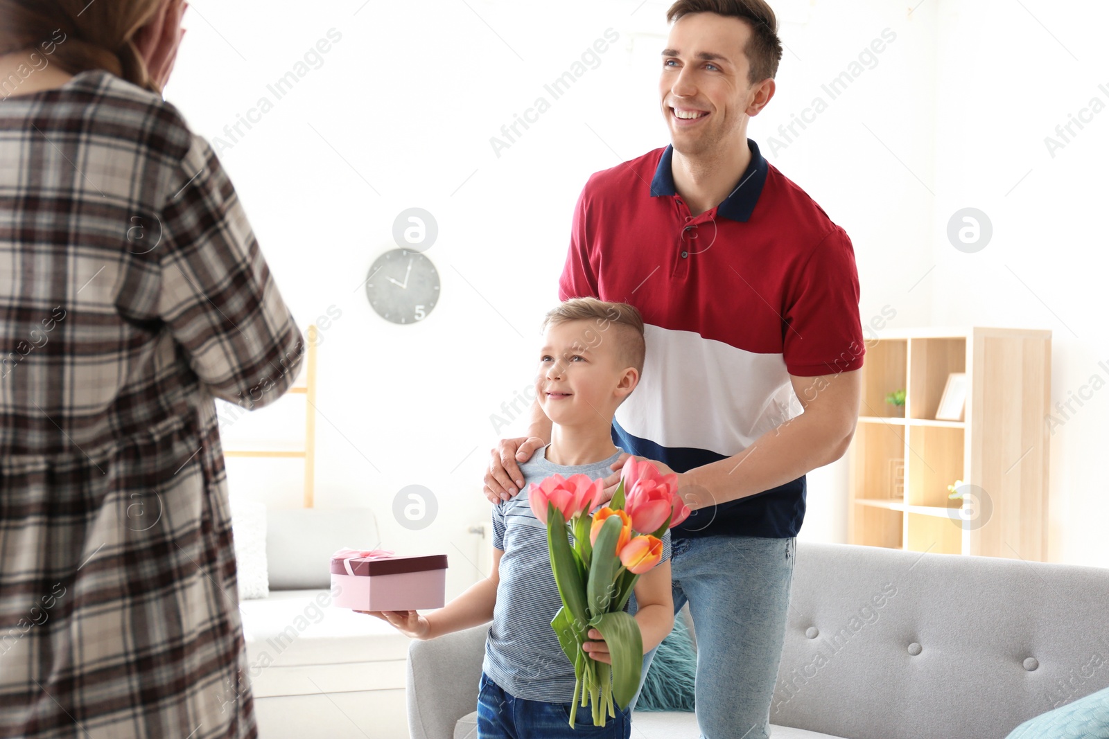 Photo of Happy woman receiving flowers and gift from her family at home. Mother's day celebration