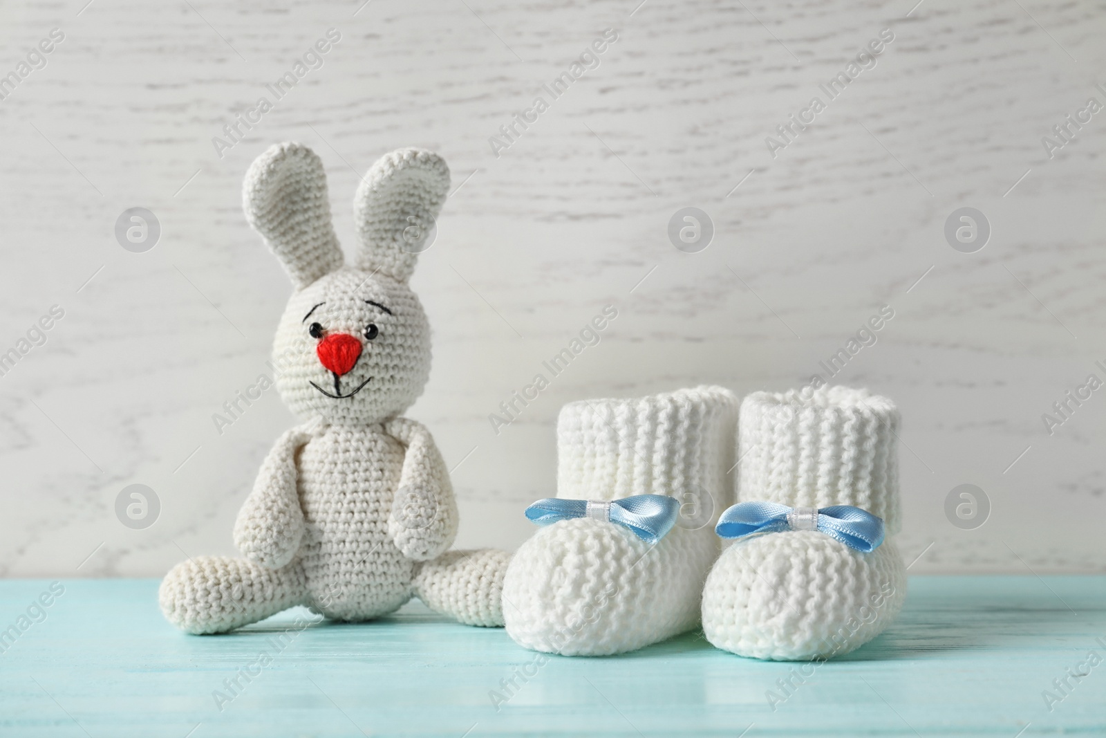 Photo of Handmade baby booties and stuffed rabbit on table against wooden background