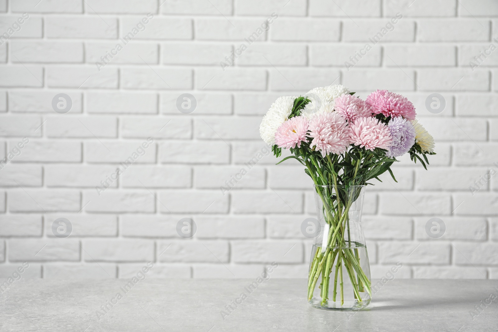 Photo of Vase with beautiful aster flower bouquet on table against brick wall. Space for text