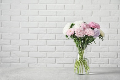 Vase with beautiful aster flower bouquet on table against brick wall. Space for text