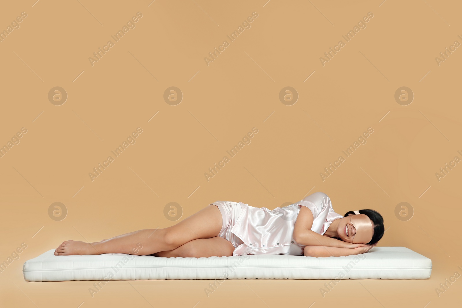 Photo of Woman with sleep mask lying on soft mattress against beige background, space for text