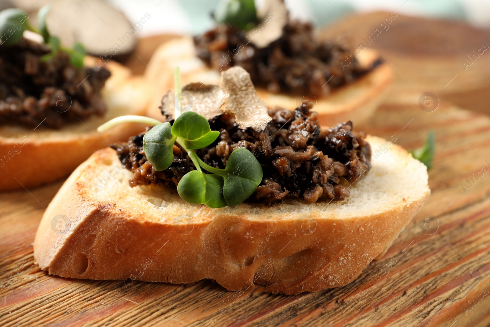 Photo of Delicious bruschetta with truffle sauce and microgreens on wooden table, closeup