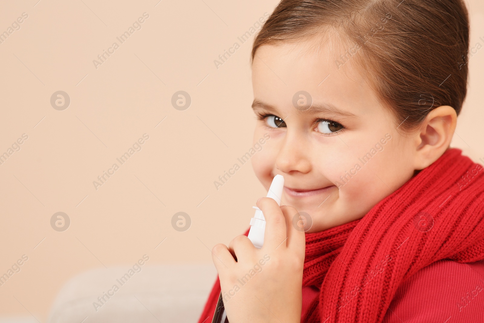 Photo of Cute little girl using nasal spray on beige background, space for text