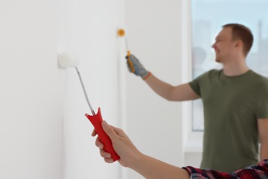 Photo of Couple painting wall in apartment during repair, closeup