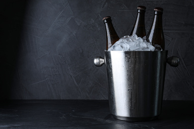 Metal bucket with beer and ice cubes on black table. Space for text