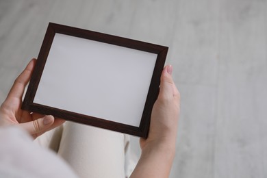 Woman holding empty photo frame indoors, closeup