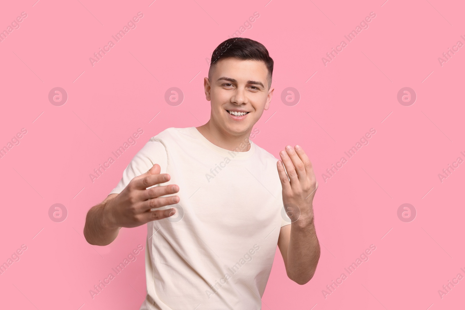 Photo of Handsome man inviting to come in against pink background