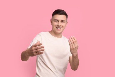 Handsome man inviting to come in against pink background