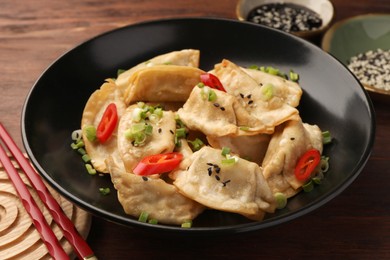 Delicious gyoza (asian dumplings) with sesame seeds, green onions and chili peppers on table