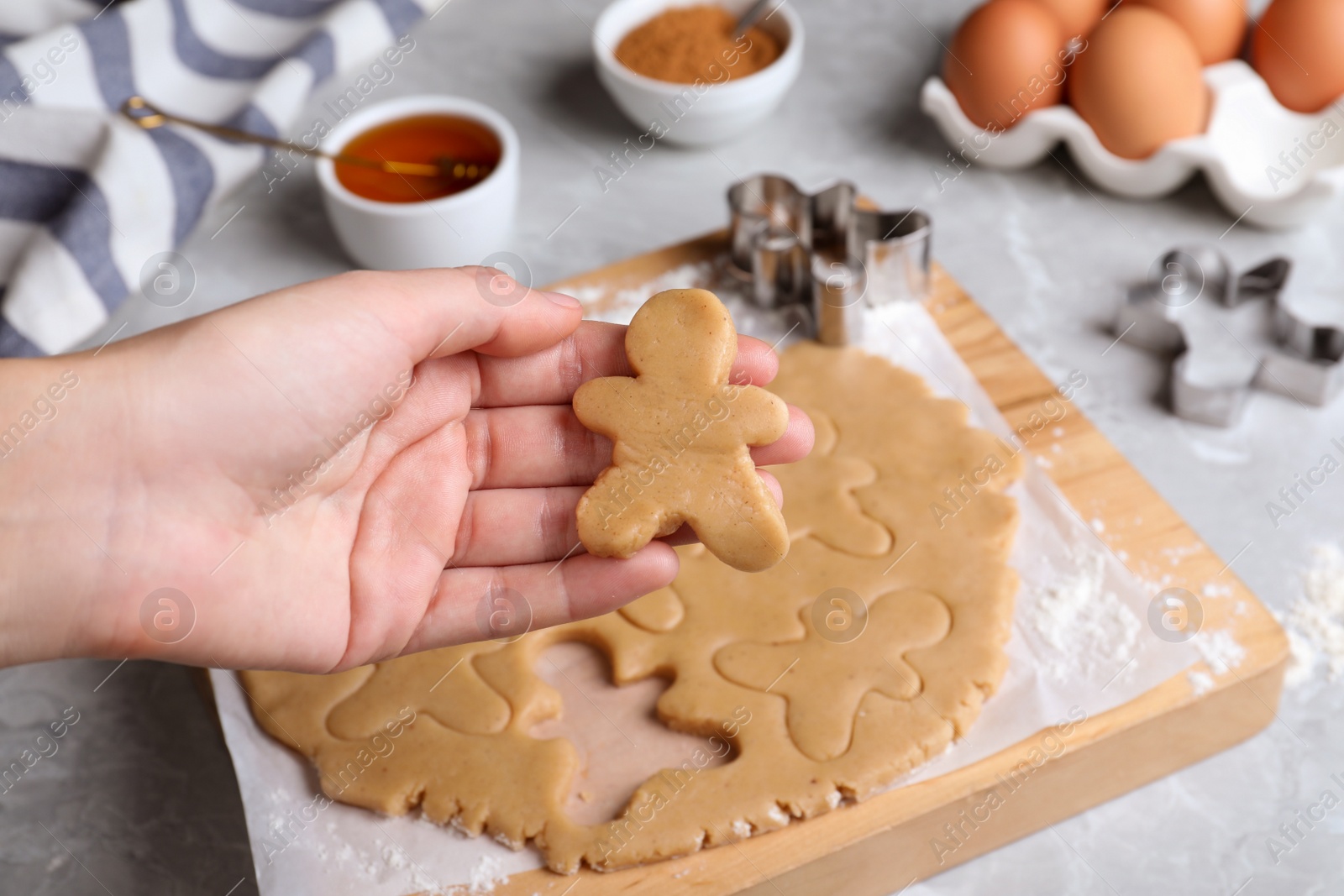 Photo of Making homemade Christmas cookies. Woman holding gingerbread man above light grey marble table, closeup