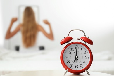 Photo of Analog alarm clock and blurred woman on background. Time of day