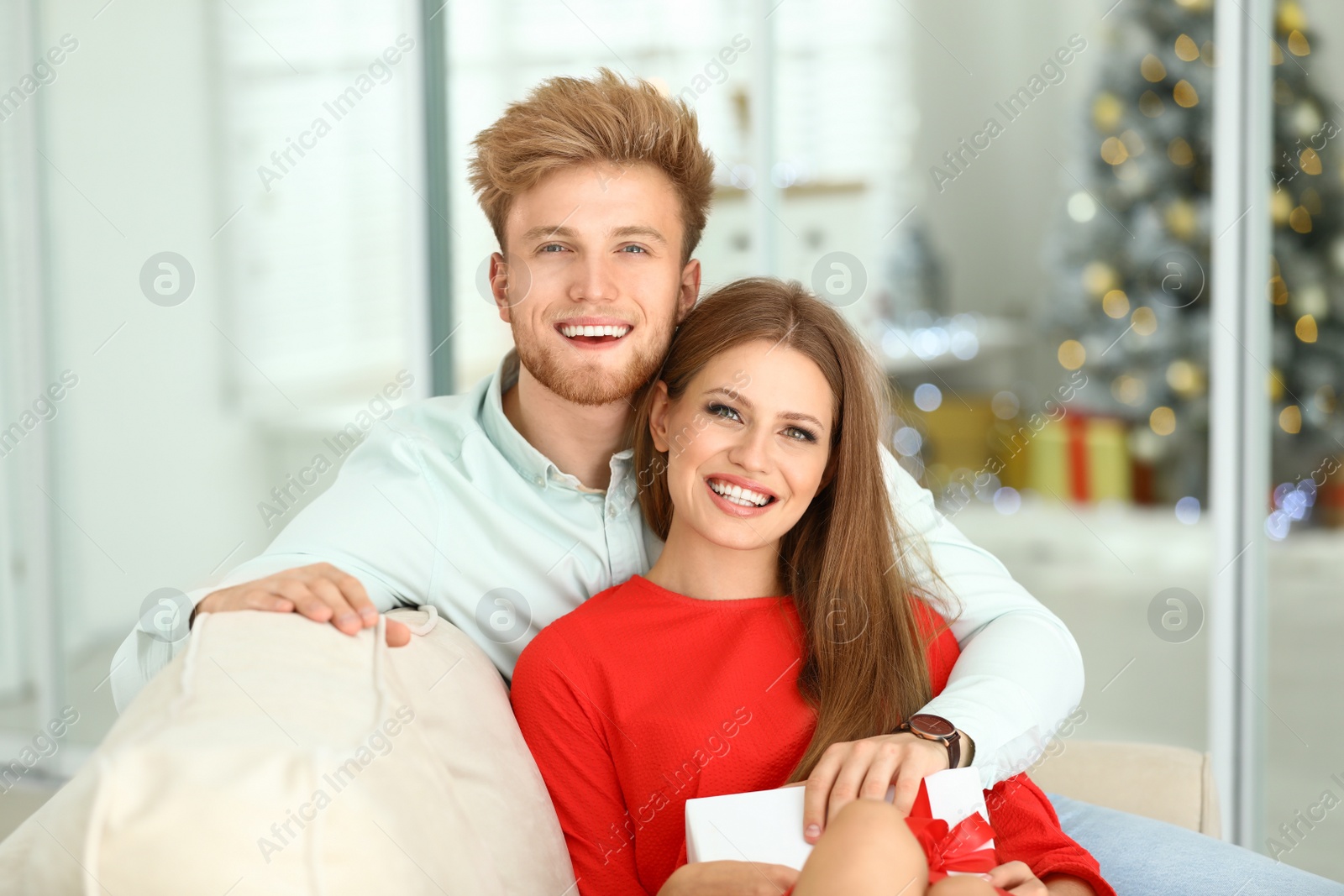 Photo of Happy young couple with Christmas gift on sofa at home