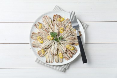 Photo of Tasty pickled anchovies with spices and fork on white wooden table, top view