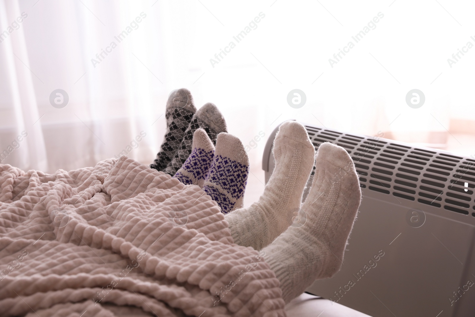 Photo of Family warming feet near electric heater at home, closeup