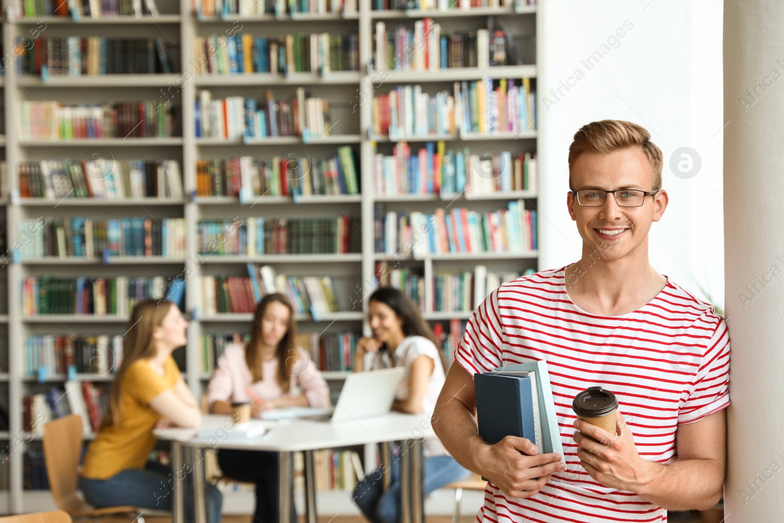 Photo of Young man with books and drink in library. Space for text