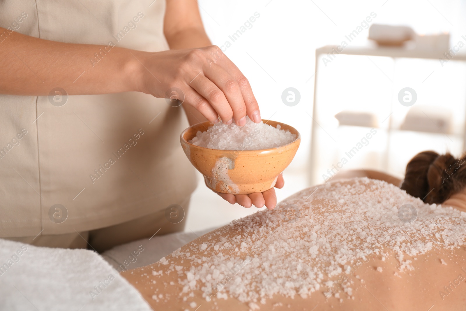 Photo of Young woman having body scrubbing procedure with sea salt in spa salon, closeup