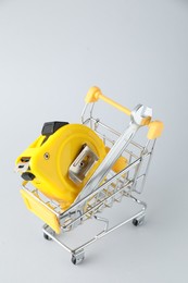 Photo of Metal wrench and measuring tape in shopping cart on light grey background