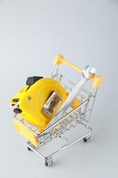 Metal wrench and measuring tape in shopping cart on light grey background