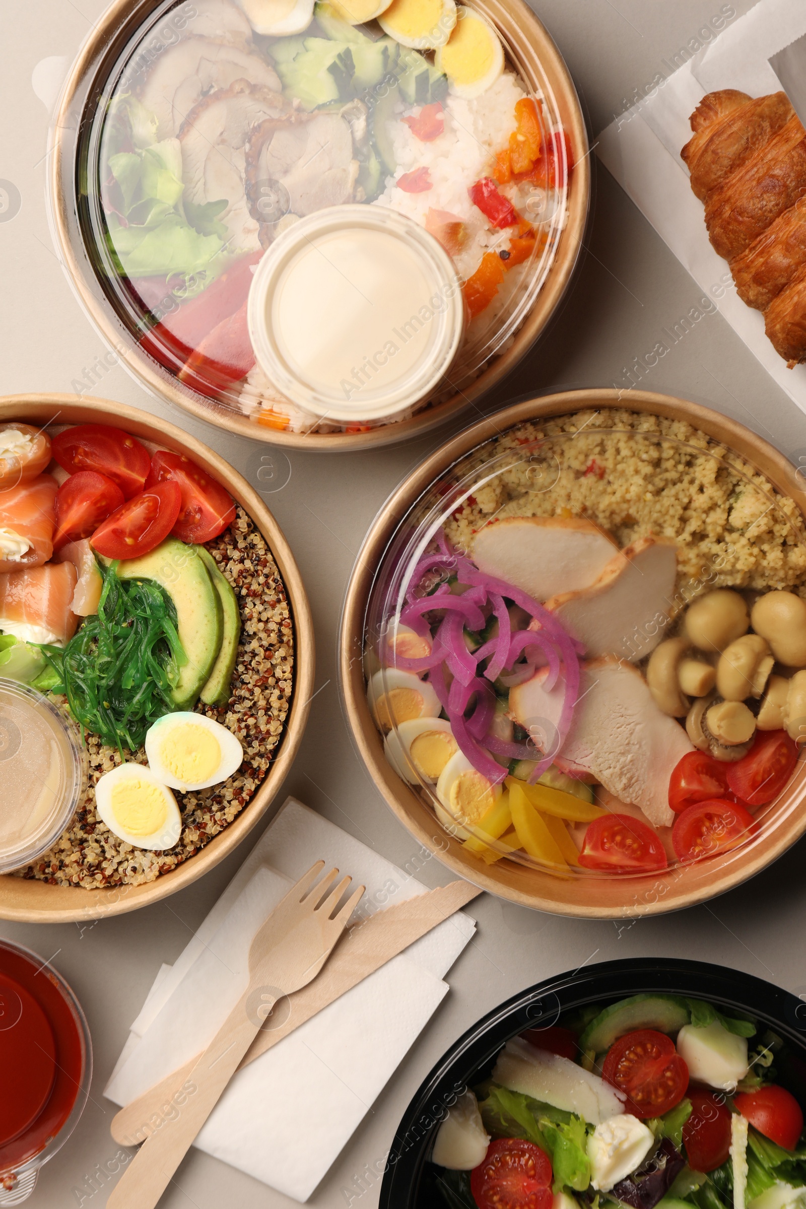 Photo of Tasty food in containers with wooden knife and fork on light grey table, flat lay