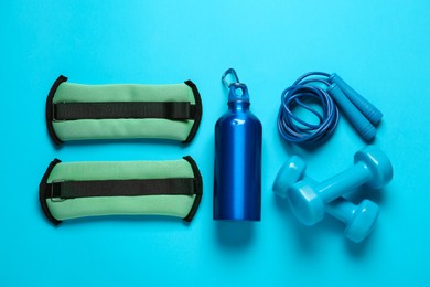 Photo of Turquoise weighting agents and sport equipment on light blue background, flat lay