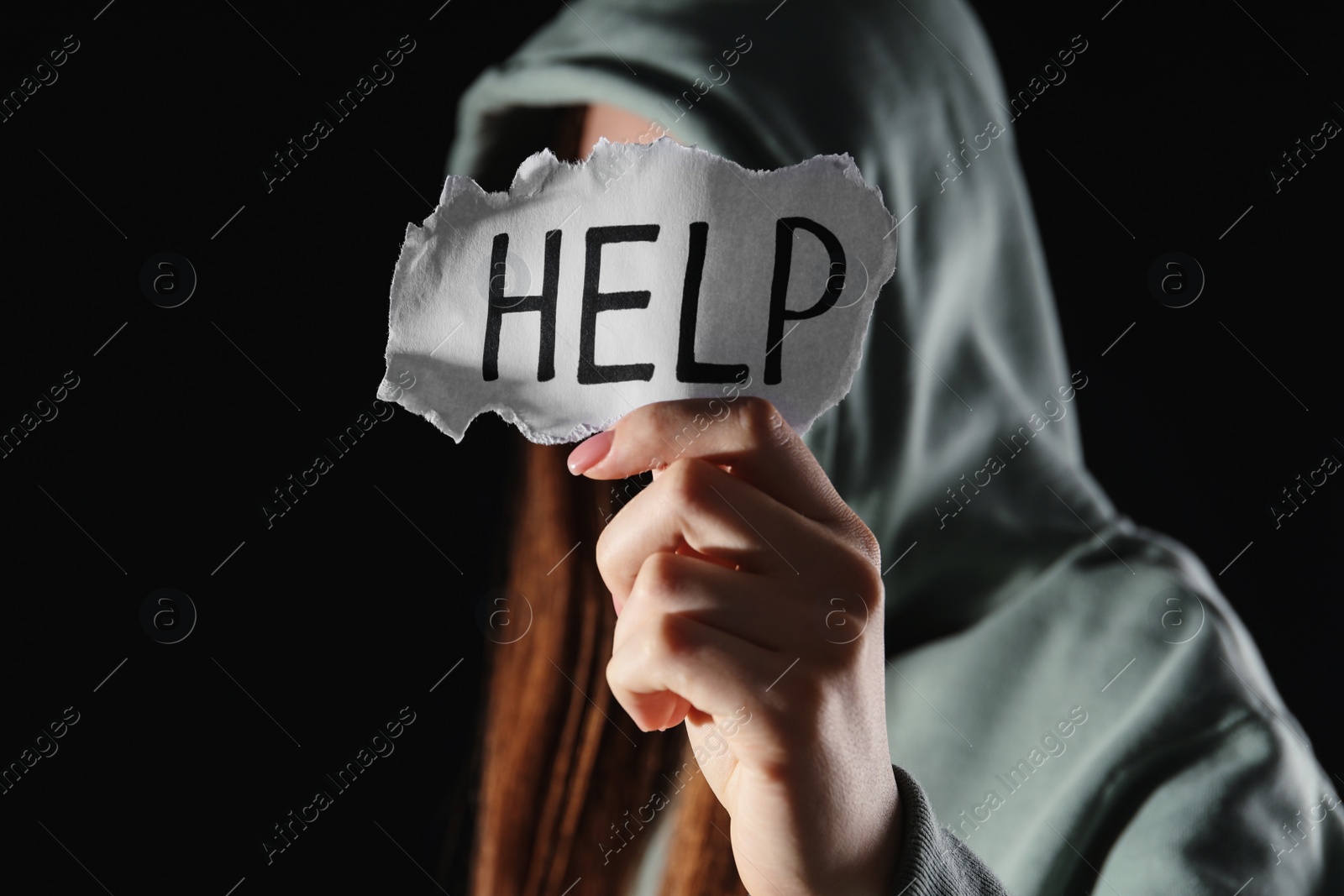 Photo of Woman holding piece of paper with word Help on black background, closeup. Domestic violence concept