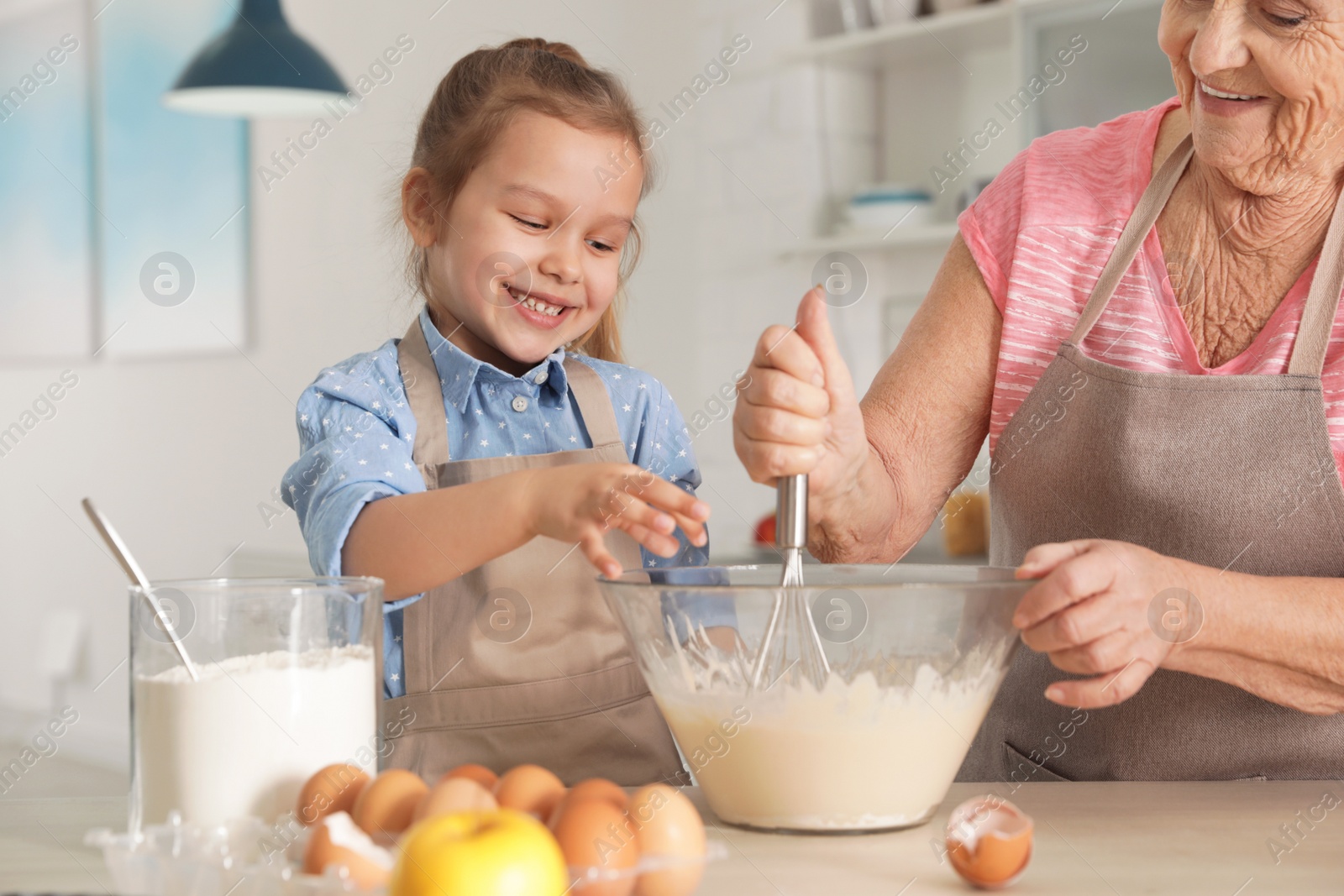 Photo of Cute girl and her grandmother cooking in kitchen