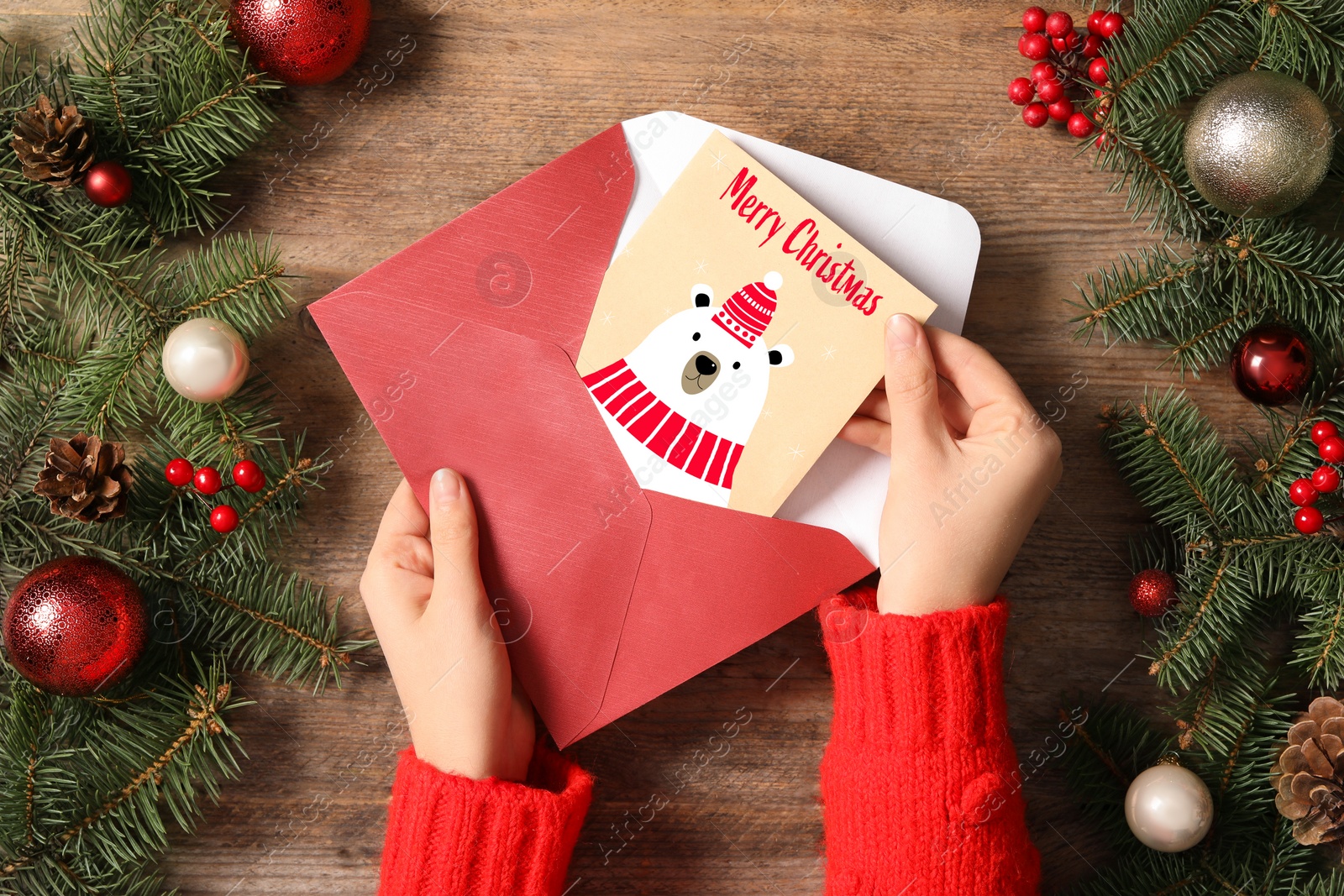 Image of Woman taking greeting card with text Merry Christmas from envelope at wooden table, top view