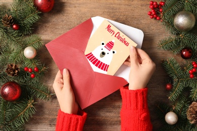 Image of Woman taking greeting card with text Merry Christmas from envelope at wooden table, top view