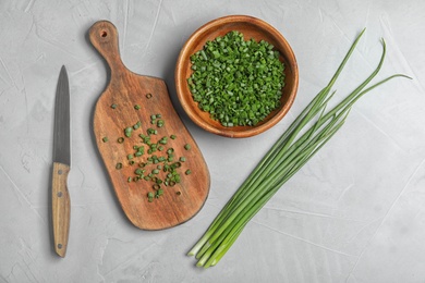 Photo of Flat lay composition with green onions, knife and bowl on grey stone table