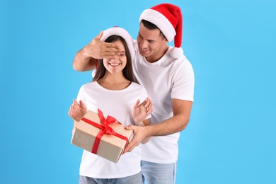 Photo of Man presenting Christmas gift to his girlfriend on light blue background