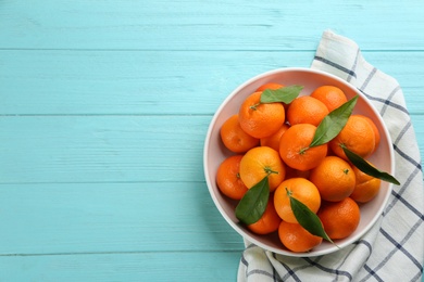 Photo of Fresh ripe tangerines with green leaves on light blue wooden table, flat lay. Space for text