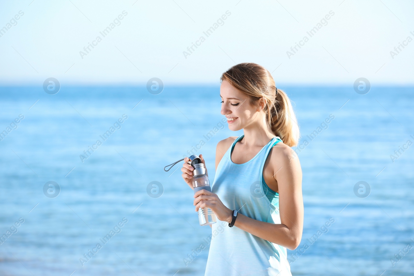 Photo of Young woman holding bottle with water on beach. Morning workout