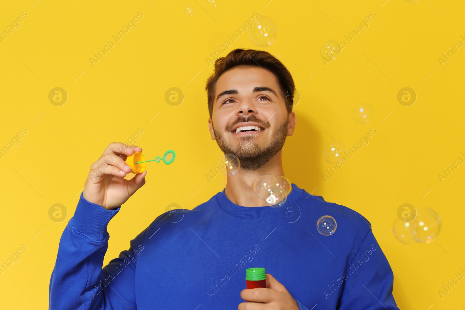 Photo of Young man blowing soap bubbles on color background