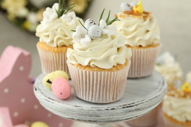 Photo of Tasty Easter cupcakes with vanilla cream and candies on cake stand, closeup