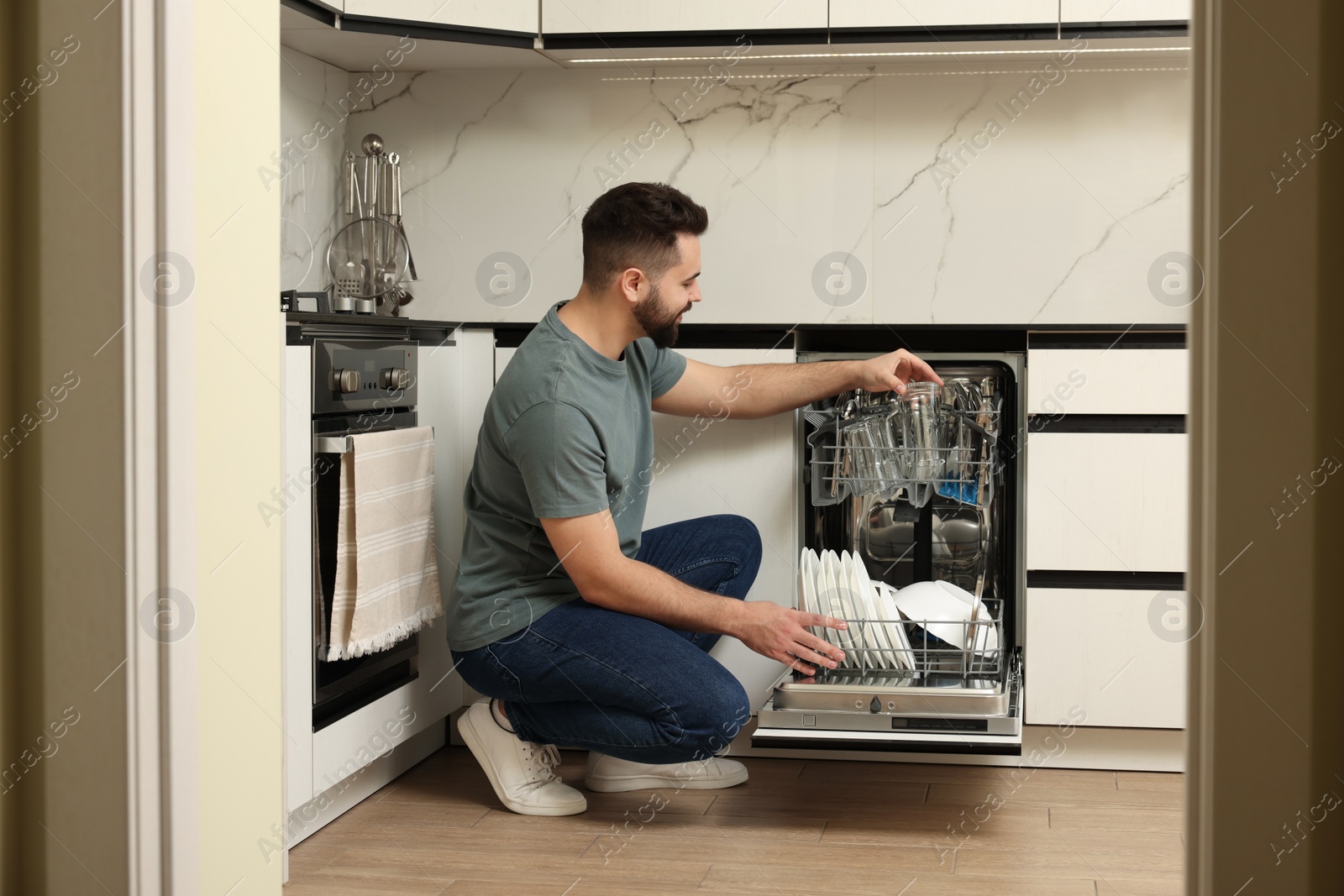 Photo of Man loading dishwasher with glasses in kitchen